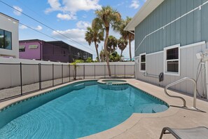 A swimming pool with a curved design, surrounded by a white fence, and adjacent to a building with a grey exterior. - Beach Bungalow- Perfect duplex for larger families (Fort Myers Beach)