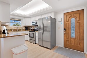 A modern kitchen with white cabinetry, stainless steel appliances, and a wooden door with a decorative glass panel. - Beach Bungalow- Perfect duplex for larger families (Fort Myers Beach)
