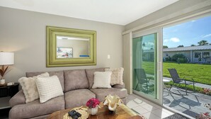 A living room with a sofa, a coffee table with remote controls, a vase of flowers, and a large mirror on the wall. - Jamaica Royale #11- Everything NEW, 3 Heated Pools, Right on the Beach! (Siesta Key)
