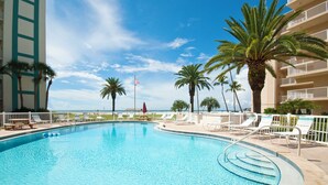 A swimming pool with lounge chairs and palm trees, surrounded by a fence and a building with balconies. - Jamaica Royale #11- Everything NEW, 3 Heated Pools, Right on the Beach! (Siesta Key)