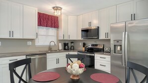 A modern kitchen with white cabinets, stainless steel appliances, a red window valance, and a dining table with pink placemats. - Jamaica Royale #11- Everything NEW, 3 Heated Pools, Right on the Beach! (Siesta Key)