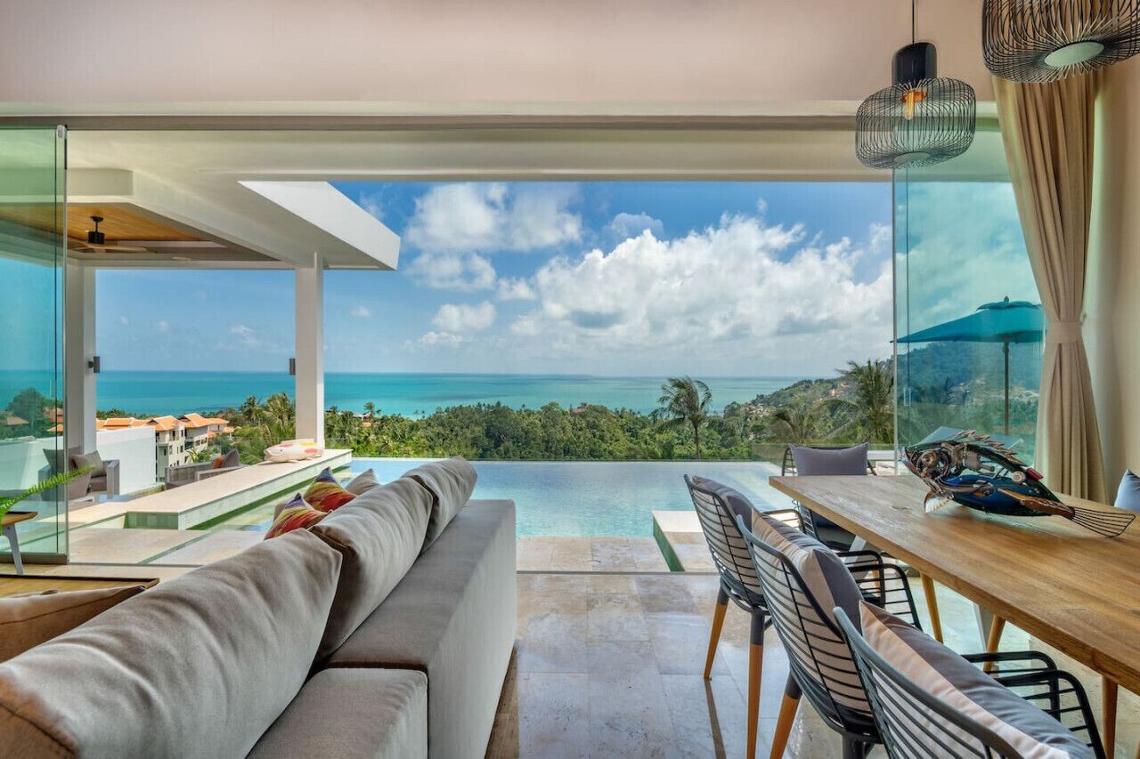A modern living room with a large glass wall offering a view of the ocean and a pool.