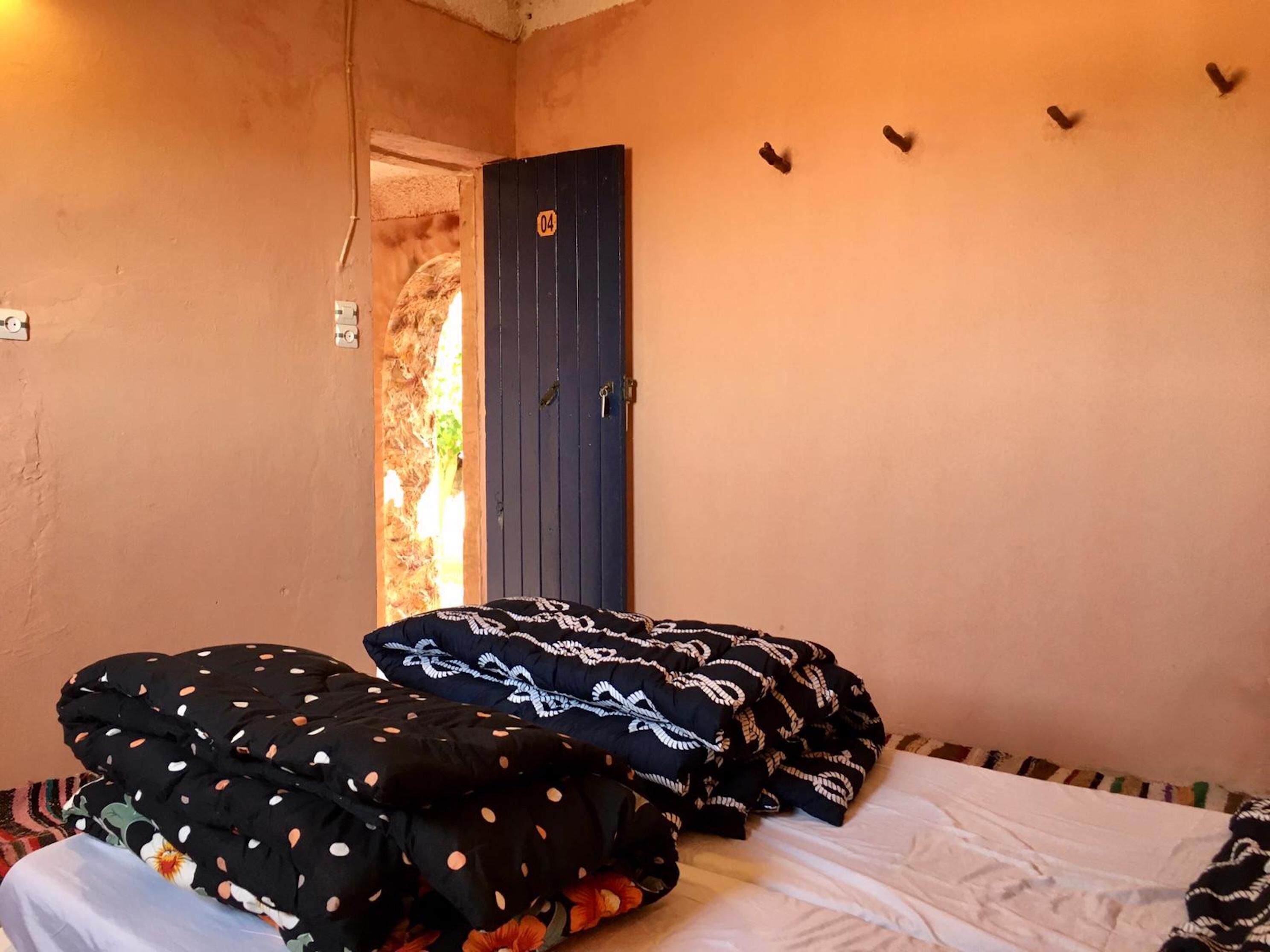 A bedroom with a bed, pillows, a door, and a wall-mounted light fixture.