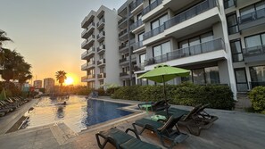 A swimming pool with lounge chairs and umbrellas, surrounded by a modern building with balconies. - Ethica Suite Luxury Houses (Antalya)