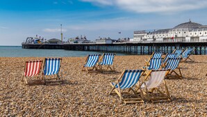 A pebbled beach with striped beach chairs and a pier with buildings in the background. - Pittodrie Guest House - Room 2 (Brighton)