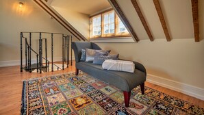 A cozy room with a gray sofa, patterned rug, wooden beams, and a window with blinds.
