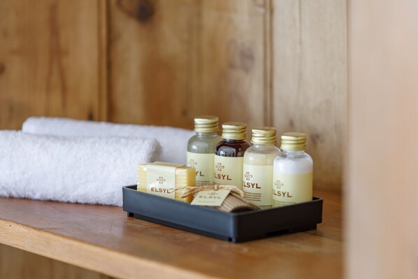 A tray with bottles and a bar of soap labeled "ELSYL" on a wooden surface with a white towel in the background.