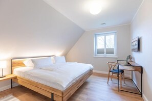 A bedroom with a wooden bed, a desk, and a chair. - Moderne Doppelhaushälfte in Niebüll (Niebüll)