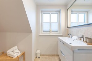 A modern bathroom with a white sink, a mirror, and a window above the sink. - Moderne Doppelhaushälfte in Niebüll (Niebüll)