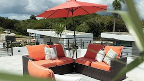 A sectional sofa with orange cushions and a red umbrella on a rooftop terrace. - Luxury home with private pool steps from Black Eagle Beach (Rincón)