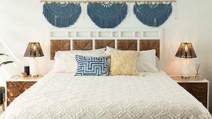A bedroom with a large bed, two bedside tables with lamps, a wooden headboard, and three macramé wall hangings. - Luxury home with private pool steps from Black Eagle Beach (Rincón)