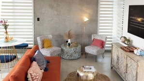 A modern living room with a sofa, two patterned armchairs, a round coffee table, a floor lamp, and a cabinet with decorative items. - Luxury home with private pool steps from Black Eagle Beach (Rincón)