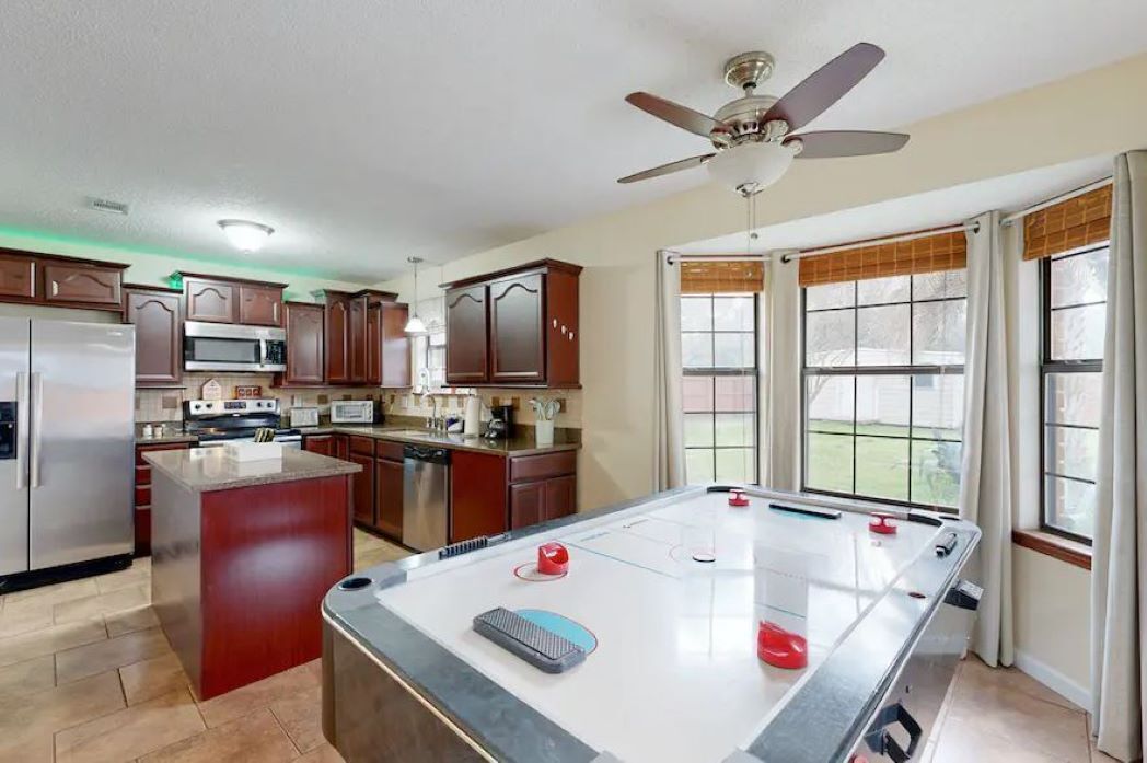 A kitchen with a pool table, wooden cabinets, a microwave, and a ceiling fan.