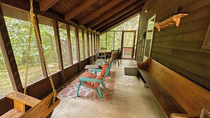 Une véranda abritée, dotée de bancs et de chaises en bois, d’une balançoire et offrant une vue sur la verdure environnante.