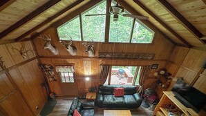 L’intérieur d’une cabane avec un plafond mansardé, des murs en bois, un canapé en cuir noir, une table basse en bois et des têtes de cerf fixées au mur.