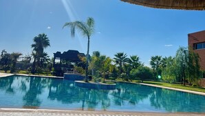 A clear blue sky, a swimming pool, and a thatched roof structure. - Domaine Bahi (Oulad Hassoune)