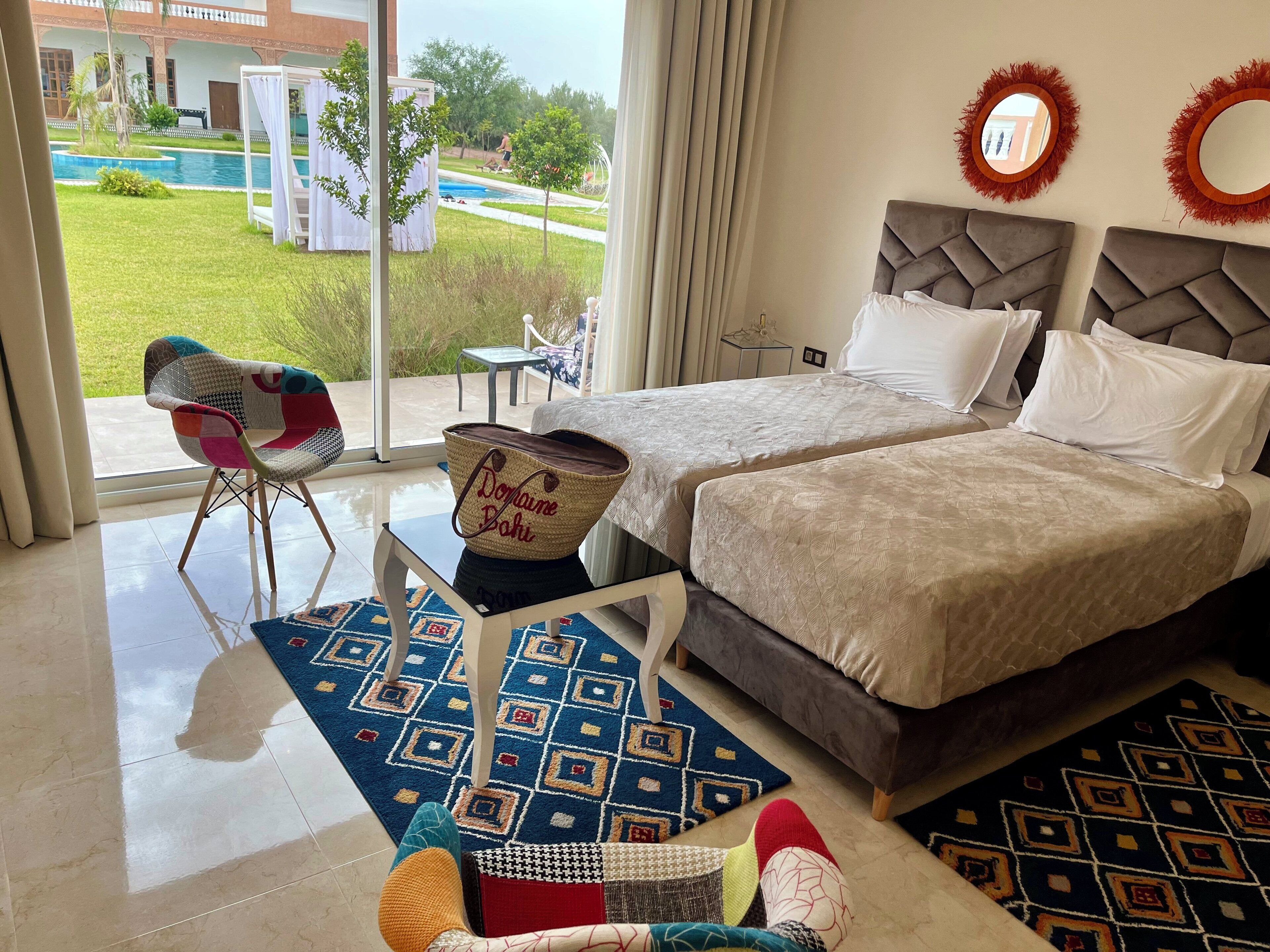 A hotel room with two beds, a view of the pool, and a balcony with a chair.