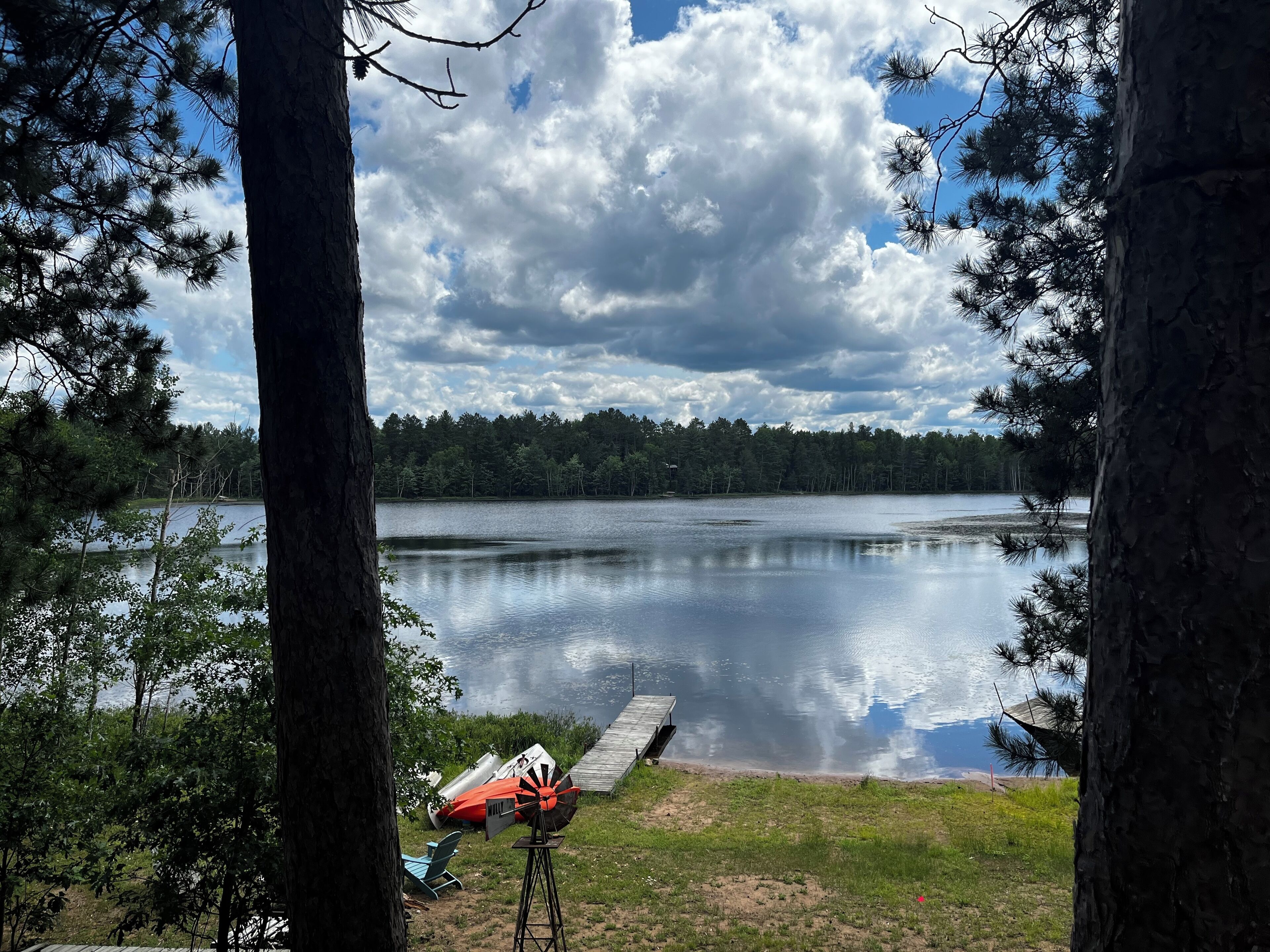 Una vista tranquila sobre un lago con un molino, un muelle y una silla junto al agua.