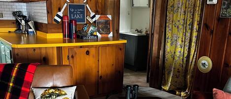 Una sala de estar acogedora con un sofá de cuero marrón, un sillón azul y un sofá gris. Se observa un mueble de madera y una encimera amarilla al fondo.