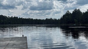 Un muelle de madera se adentra en un lago tranquilo con un bosque al fondo.