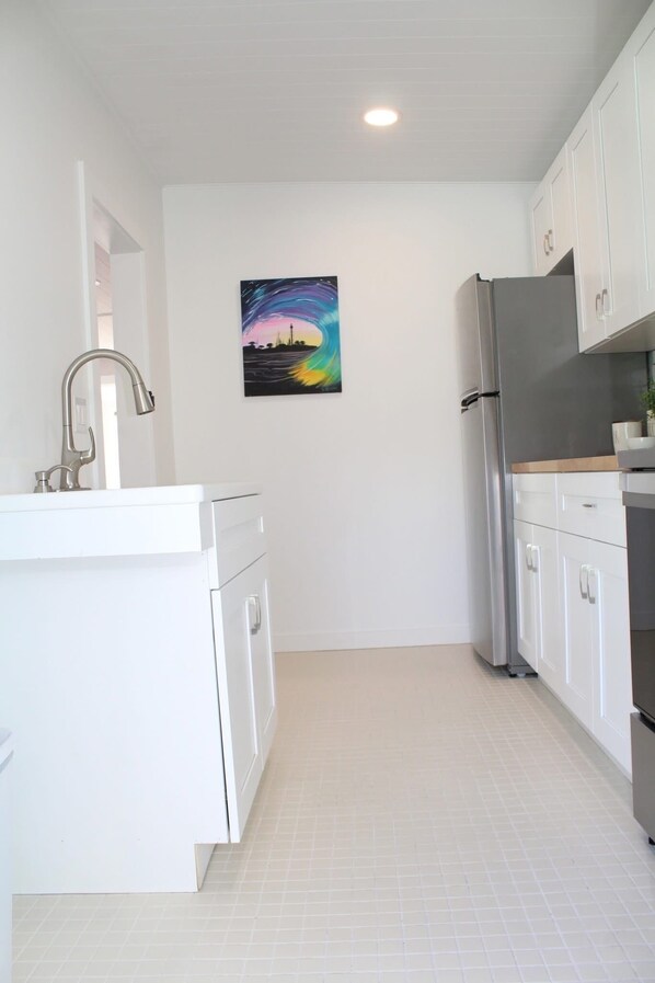A kitchen with white cabinets, a stainless steel refrigerator, and a painting on the wall. - Anclote River casita, vacation rental.Tarpon Springs,FL (Tarpon Springs)