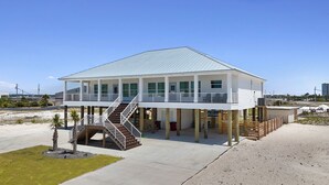 A two-story beach house with a balcony, a staircase, and a sandy surrounding. - Beautiful Beach Home Steps from the crystal blue waters of Navarre Beach! (Navarre)