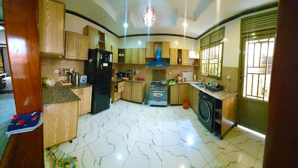 A kitchen with wooden cabinets, a black refrigerator, a stove, a washing machine, and a window with bars.