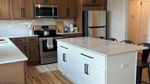 A modern kitchen with wooden cabinets, stainless steel appliances, a marble countertop, and a central island.