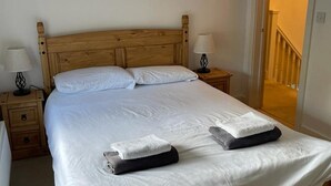 Un letto rifatto con lenzuola bianche e due asciugamani piegati, una testiera in legno, comodini con lampade e una scala che conduce a un piano superiore.