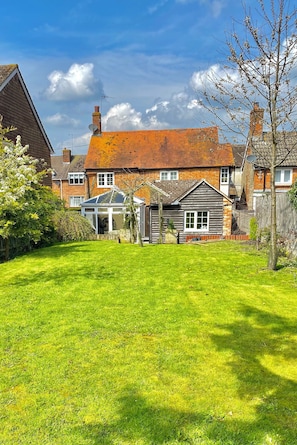 A residential property with a well-maintained lawn, a conservatory, and a brick house with a tiled roof.