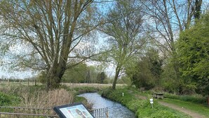 Una passeggiata lungo il fiume con ringhiera metallica e cartello segnaletico.