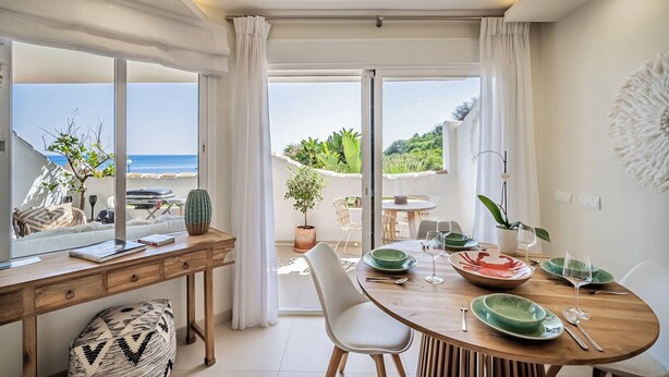 A dining area with a view of the sea, a wooden table, and a comfortable seating arrangement.