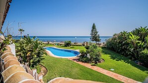 A pool surrounded by a well-maintained lawn, a clear blue sky, and a view of the sea.