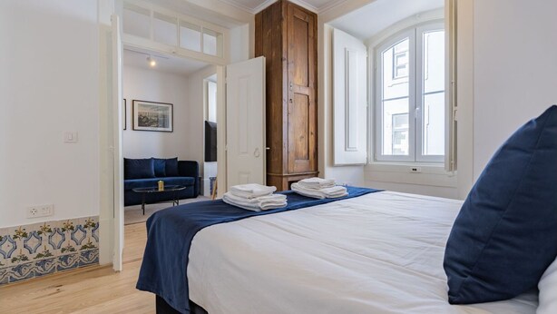 Una habitación de hotel con una cama, un sofá azul, un armario de madera y una ventana con vistas.