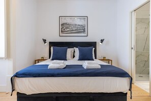 A neatly made bed with a dark headboard, two bedside tables with lamps, and a framed cityscape picture on the wall.