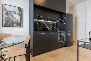 A modern kitchen with black cabinets, a glass table, and a framed cityscape picture on the wall.