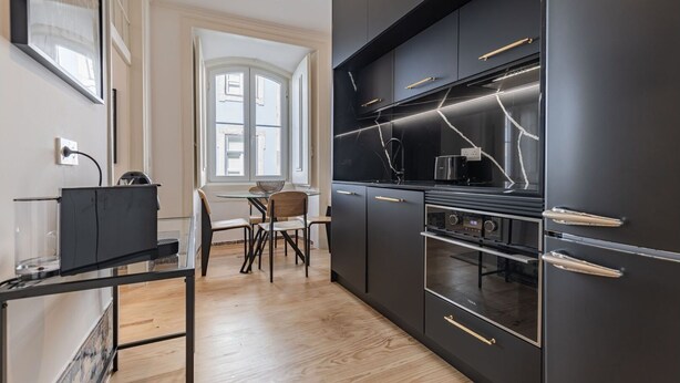 A modern kitchen with black cabinetry, a glass dining table, and a window with natural light. - Figueira Quality III by LovelyStay (Lisboa)