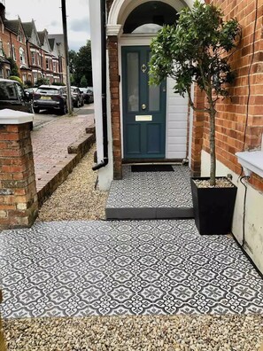 A residential entrance with a patterned tile floor, a blue door, and a small tree in a planter.