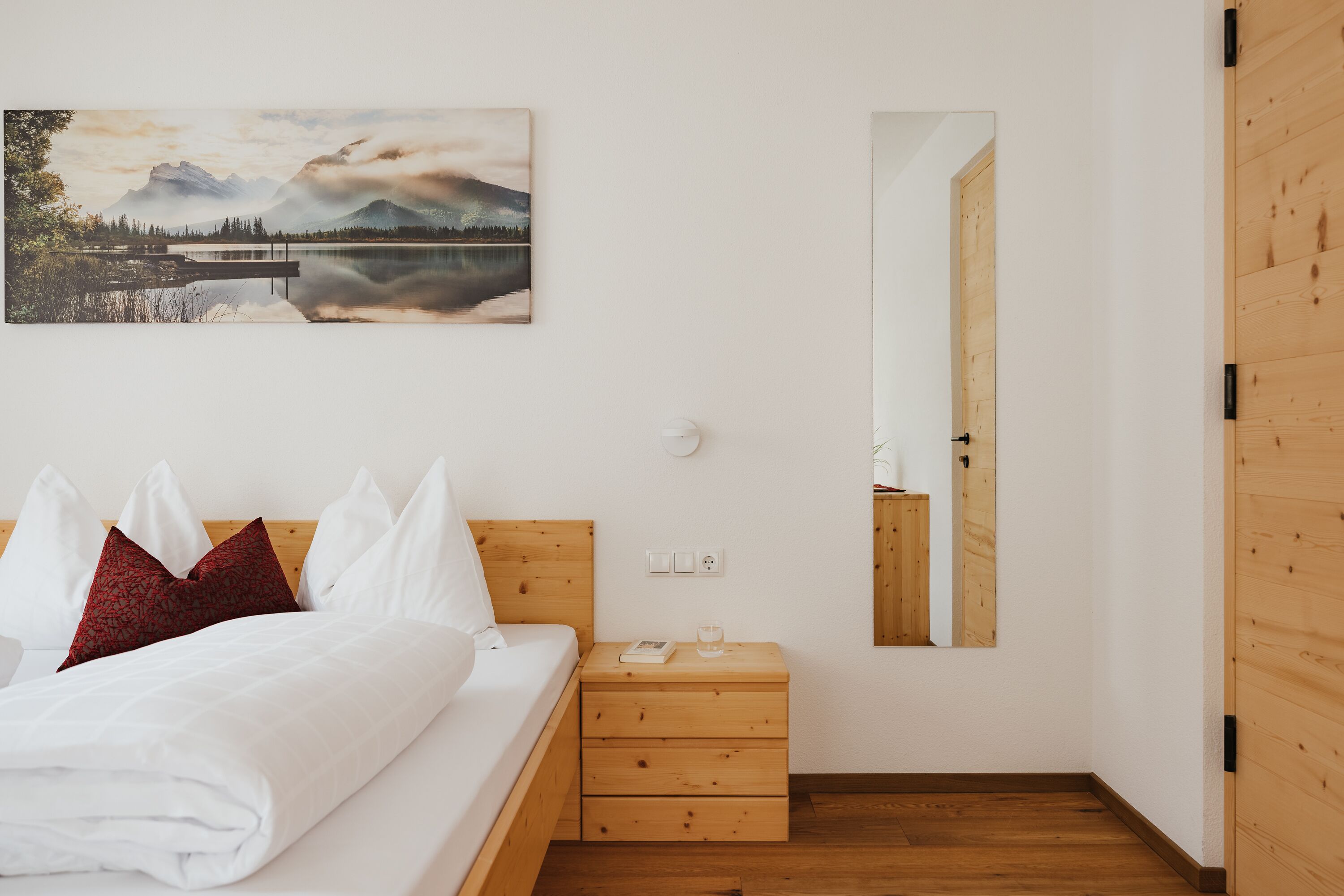 A bedroom with a bed, wooden nightstand, and a painting of a landscape.