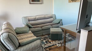 Un salon avec un canapé à rayures, un pouf assorti, une table basse en verre et un téléviseur.