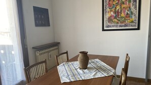 Une table à manger agrémentée d’un vase en osier, de chaises en bois, d’une nappe à motifs et d’un tableau encadré accroché au mur.