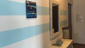 Un couloir avec un mur à rayures, un miroir et une petite table sur laquelle se trouvent un livre et un bol.