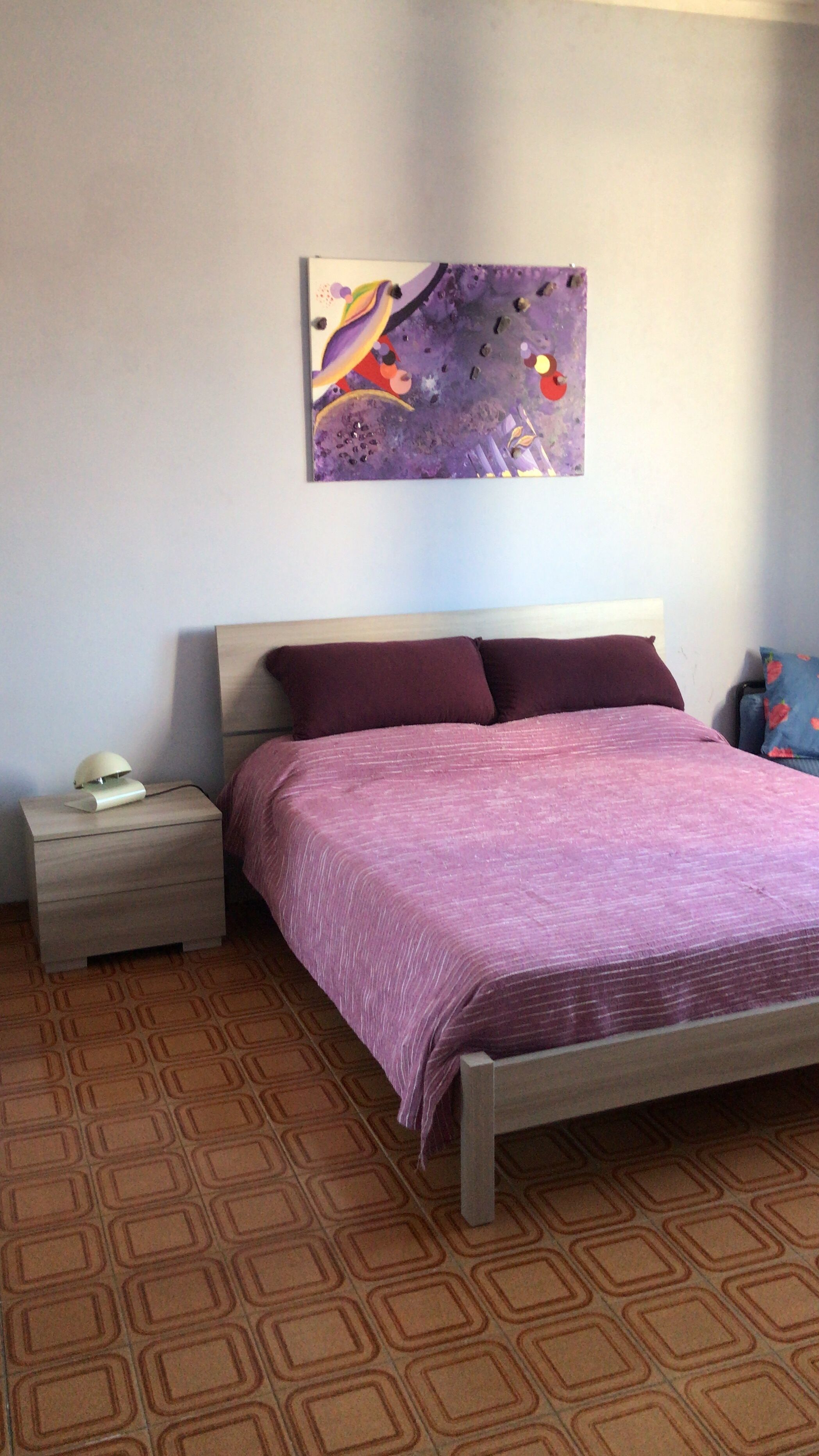 A bedroom with a bed, a nightstand, a lamp, and a wall-mounted painting.