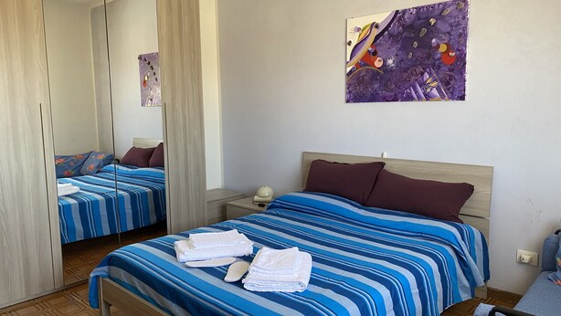 Une chambre d’hôtel avec un grand miroir, un lit avec une literie à rayures, une table de chevet avec une lampe et un tableau accroché au mur.