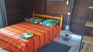 Ein Einzelbett mit gestreifter Bettdecke und zwei Kissen, ein Nachttisch mit Lampe sowie ein kleiner runder Tisch ebenfalls mit einer Lampe.