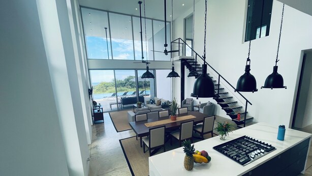 Une cuisine moderne dotée d’un îlot central, d’un coin repas offrant une vue agréable et d’un escalier menant à un balcon.
