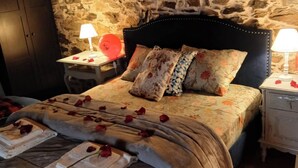 Un dormitorio con pared de piedra, una cama con colcha estampada, dos lámparas de noche y un armario de madera.