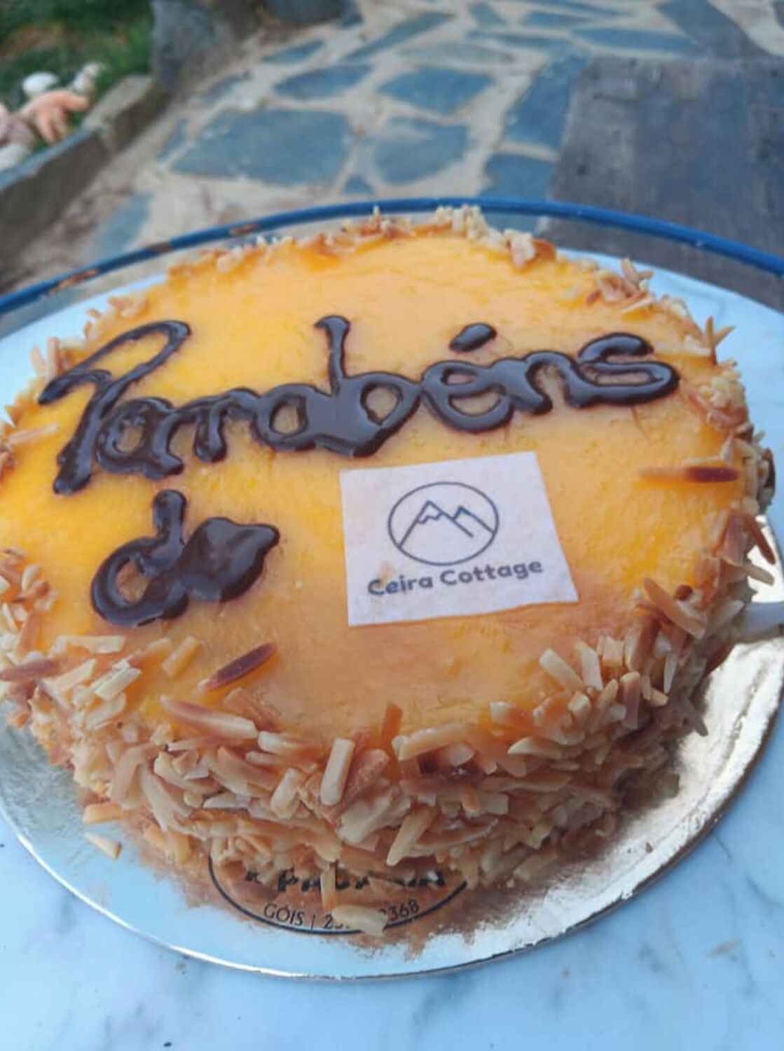 Um bolo com a inscrição 'Parbens da Ceira Cottage' sobre um prato.
