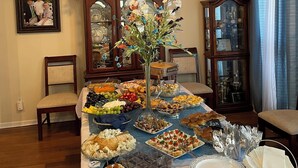 Une salle à manger avec un buffet garni de divers plats, un vase rempli de fleurs et un buffet en bois doté de portes en verre.