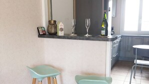 Eine Küche mit zwei hellblauen Barhocker, einem Kühlschrank und einem Fenster.